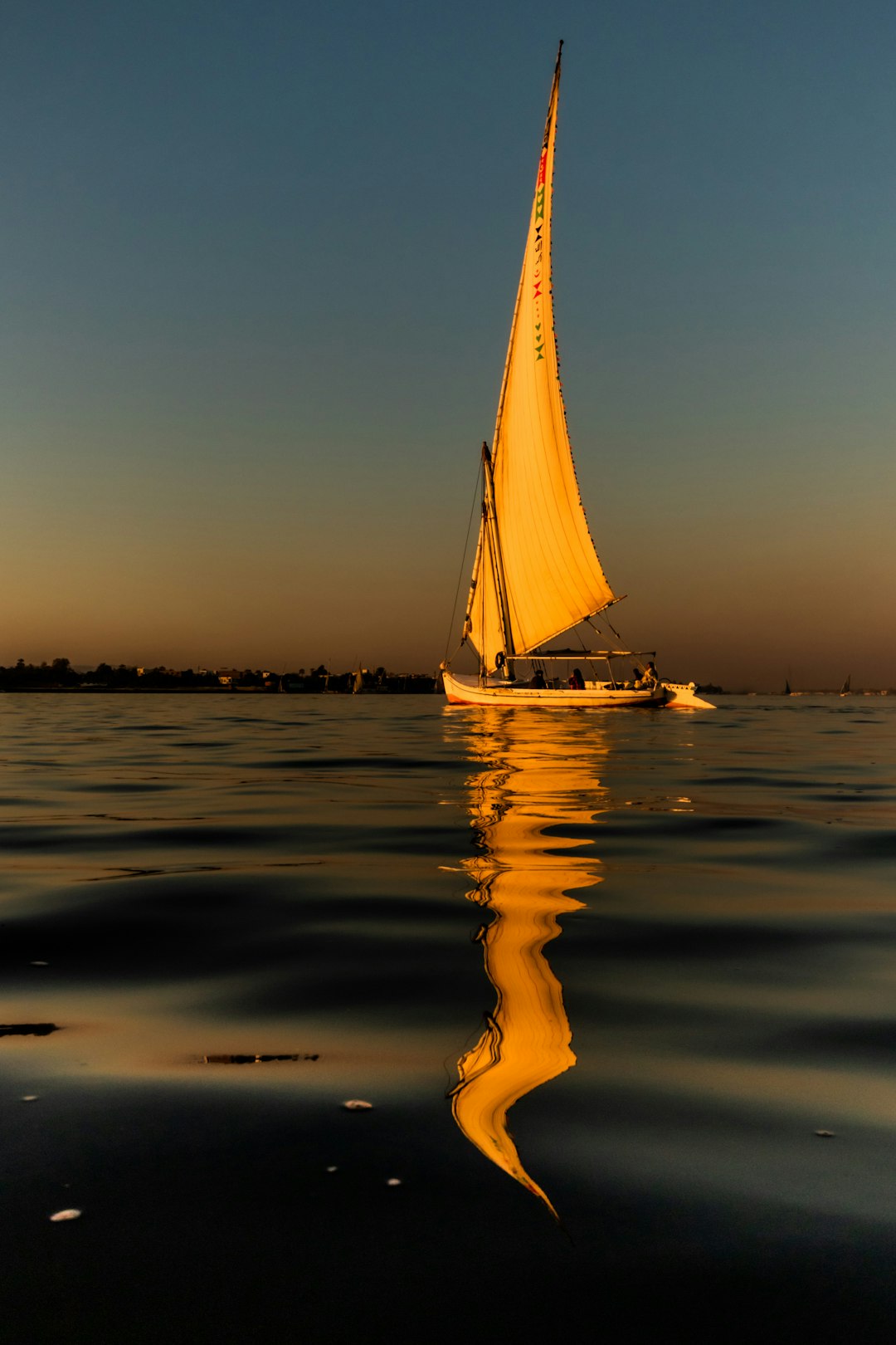A felucca sail boat on the River Nile reflected in the water.